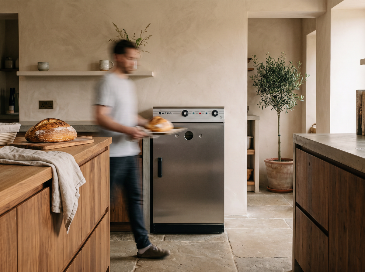 A Rofco oven in a modern, warm-toned kitchen, with a blurred person carrying bread in the background.